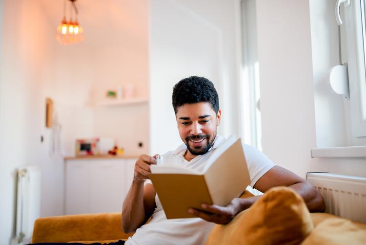 A young man sitting on a sofa reading a book.